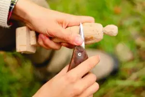 Person skillfully carving a wooden figure with a knife in a serene outdoor setting.